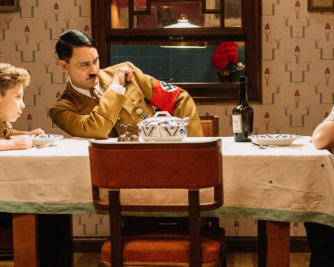 A still from the film, Jojo Rabbit. (Left to right): Jojo (Roman Griffin Davis) has dinner with his imaginary friend Adolf (Writer/Director Taika Waititi), and his mother, Rosie (Scarlet Johansson). Photo by Kimberley French. © 2018 Twentieth Century Fox Film Corporation All Rights Reserved