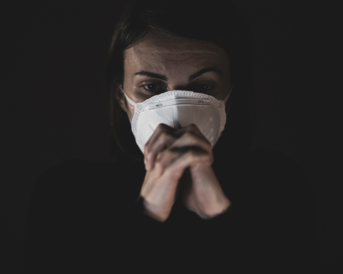 woman in mask sits in the dark with a worried look on her face. mental health