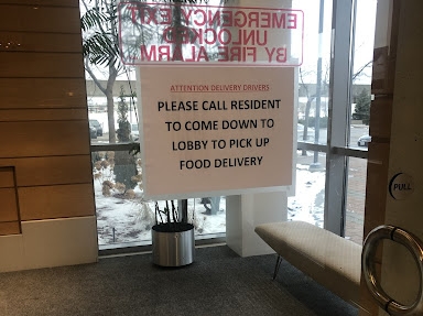 A message on the front door of a residential building that reads: "Please call resident to come down to lobby to pick up food delivery."