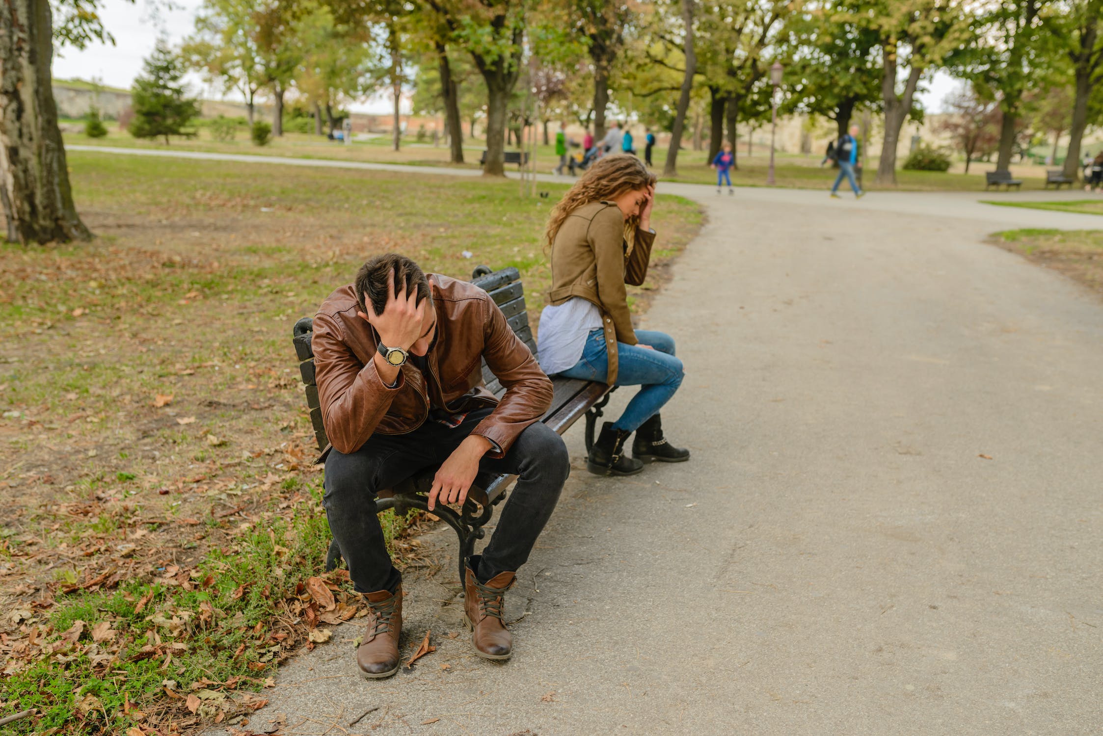A man and a woman sitting on a park bench with their heads in their hands, in a fight.