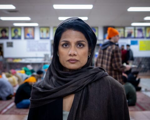 A woman wearing a black headscarf and patterned clothing looks toward the camera in a still from the film Calorie.