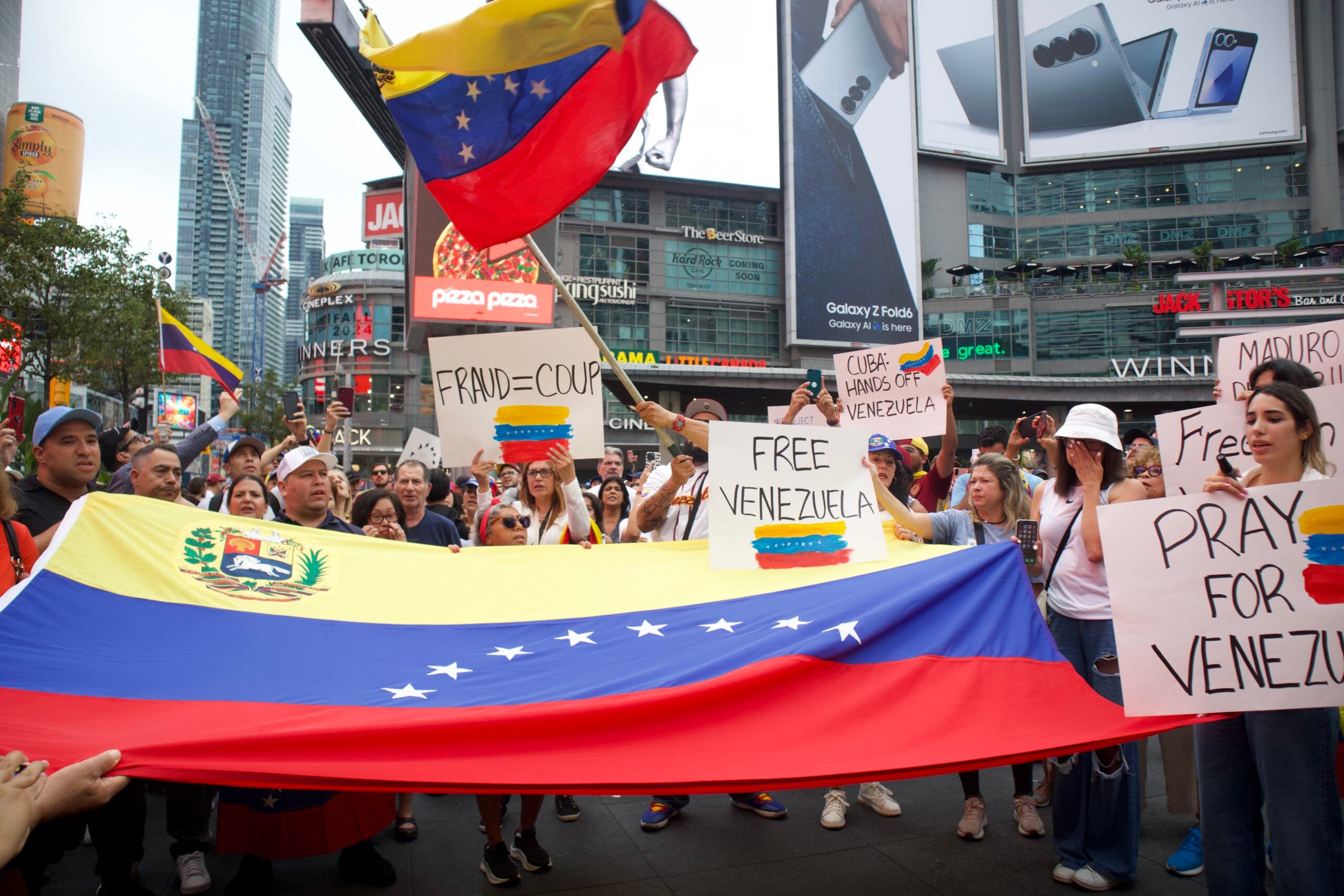 Protesters at Toronto’s Yonge-Dundas Square hold a large Venezuelan flag and signs calling for a free Venezuela.