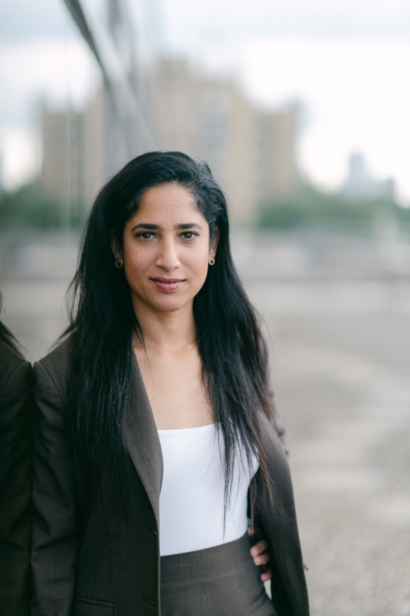 Portrait of immigration lawyer Yameena Ansari standing outdoors in a dark suit and white top, with a blurred city background.