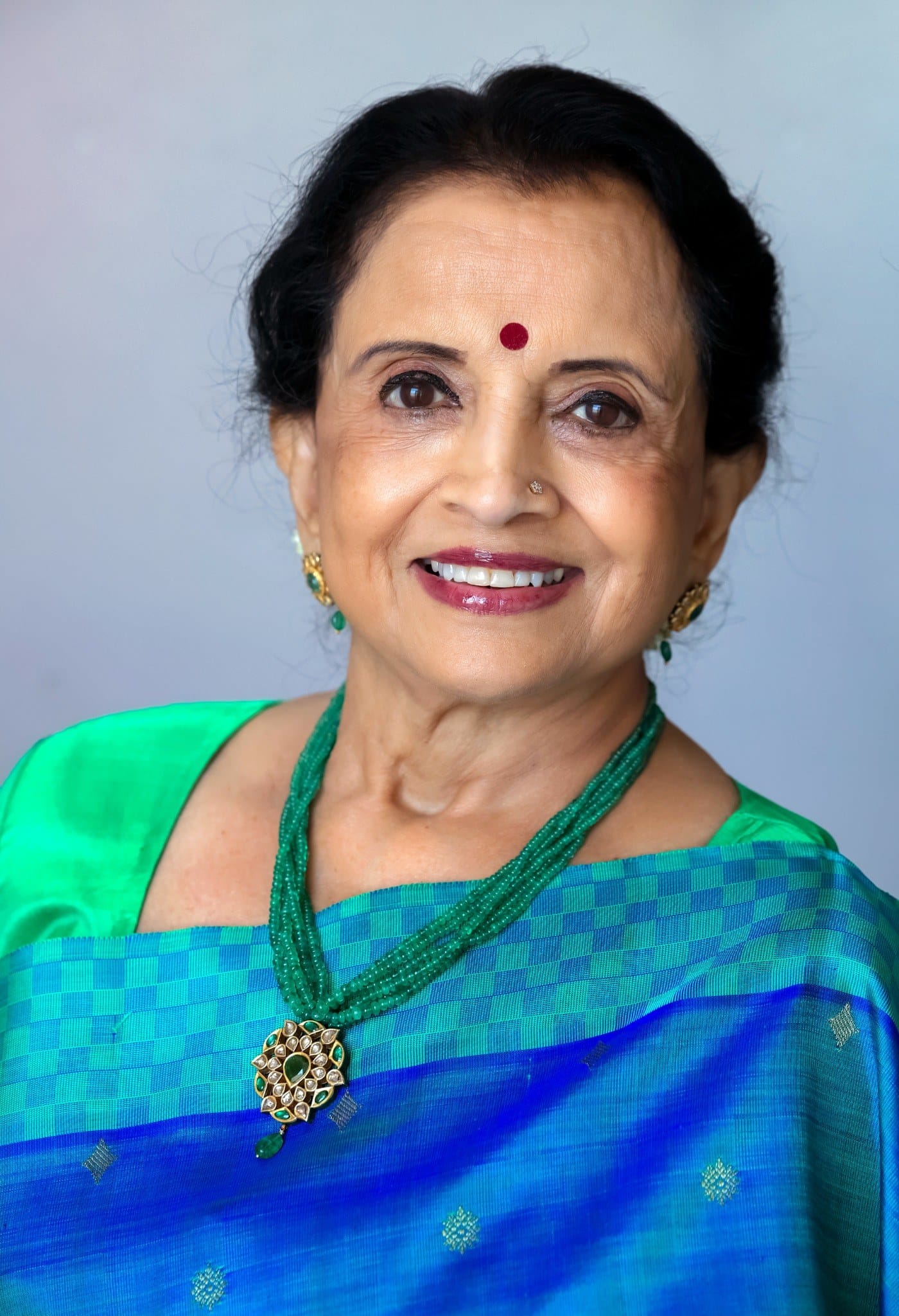 Portrait of Bharatanatyam dancer and choreographer Lata Pada wearing a blue and green sari and smiling at the camera.