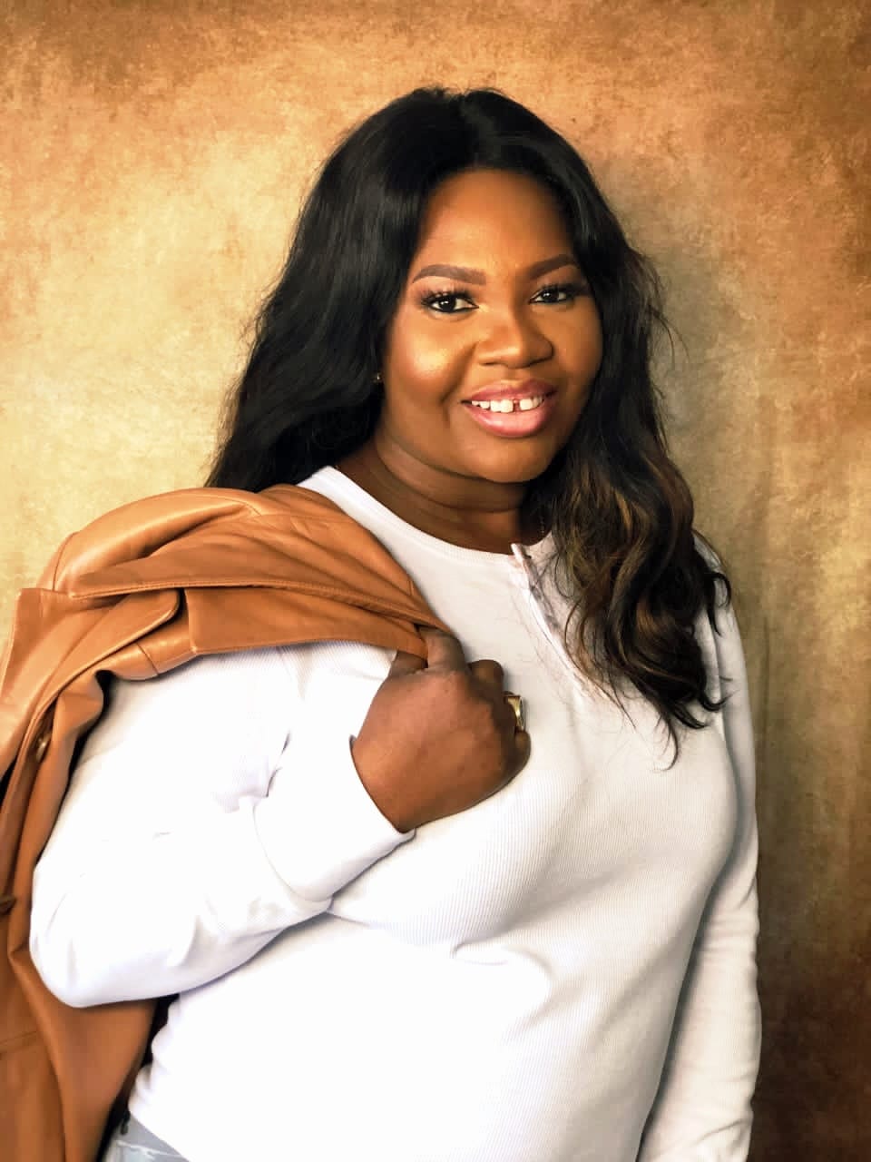 Abiodun Adetu smiles for a portrait while holding a tan jacket over her shoulder.