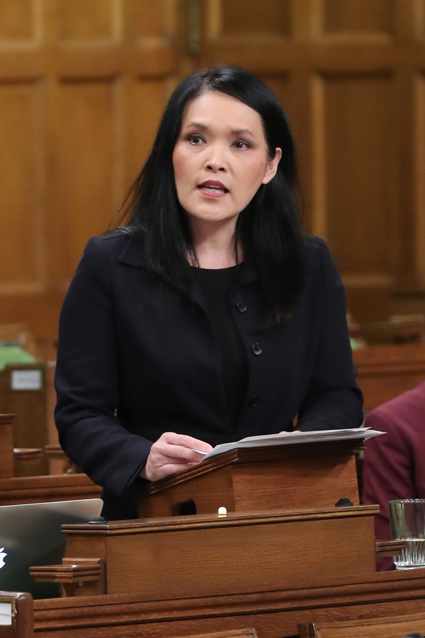 Jenny Kwan speaks in the House of Commons while holding papers at a lectern.