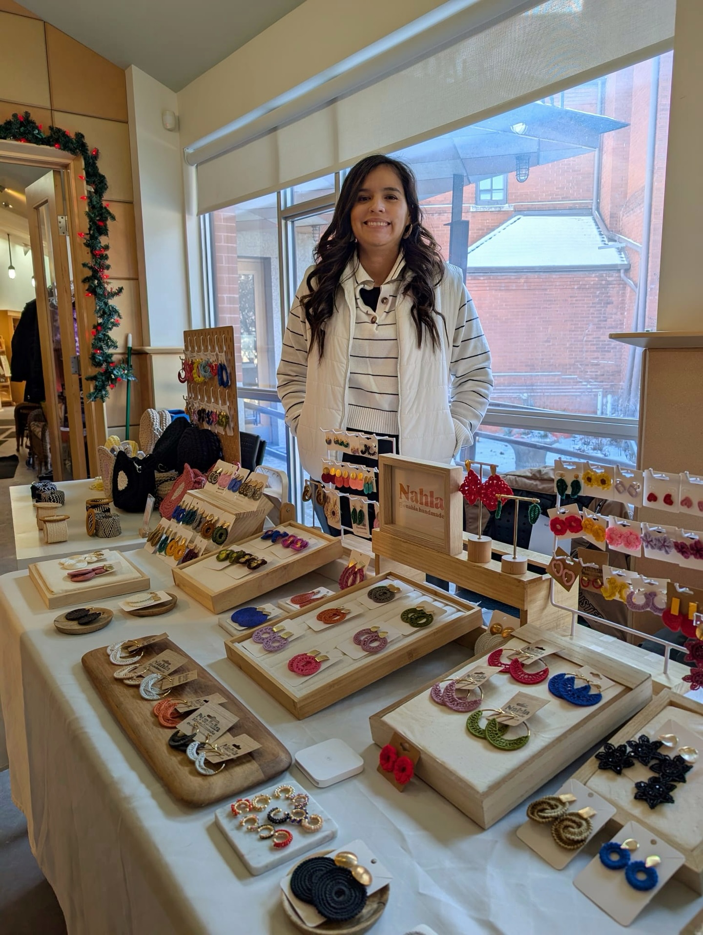 Sabrina Gomez stands behind a market table displaying handmade earrings and jewellery from Nahla Handmade.