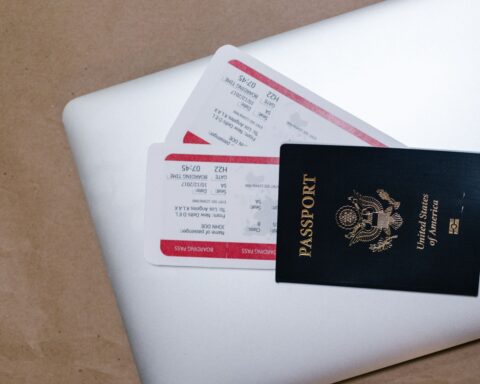 A passport and travel tickets placed on top of a laptop.
