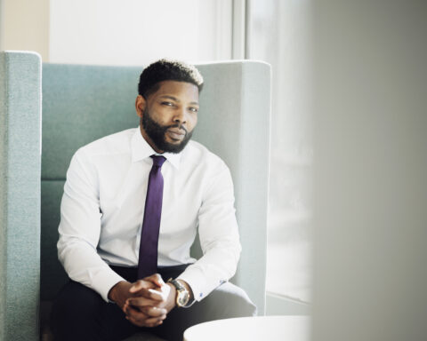 Dr. Bolu Ogunyemi, the Canadian Medical Association's first Black president, sits in an office lounge chair wearing a white dress shirt and purple tie.