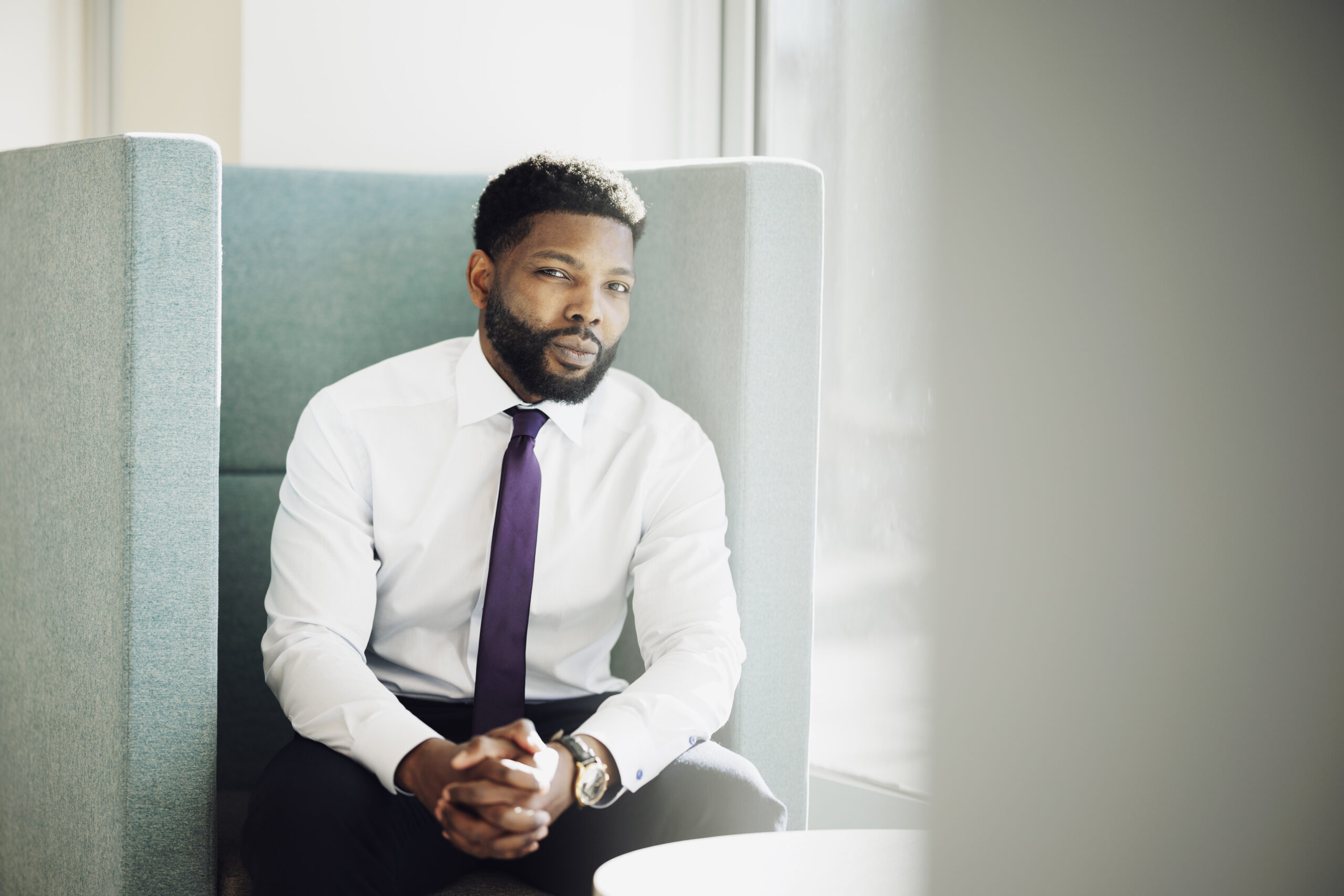 Dr. Bolu Ogunyemi, the Canadian Medical Association's first Black president, sits in an office lounge chair wearing a white dress shirt and purple tie.