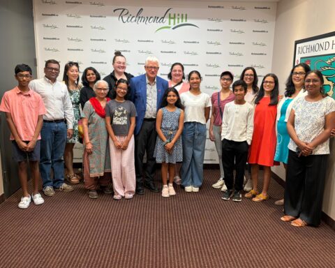 Group photo of Katya Gampa, her family, coaches and Richmond Hill Mayor David West standing together in front of a Richmond Hill step-and-repeat backdrop after a scroll presentation.
