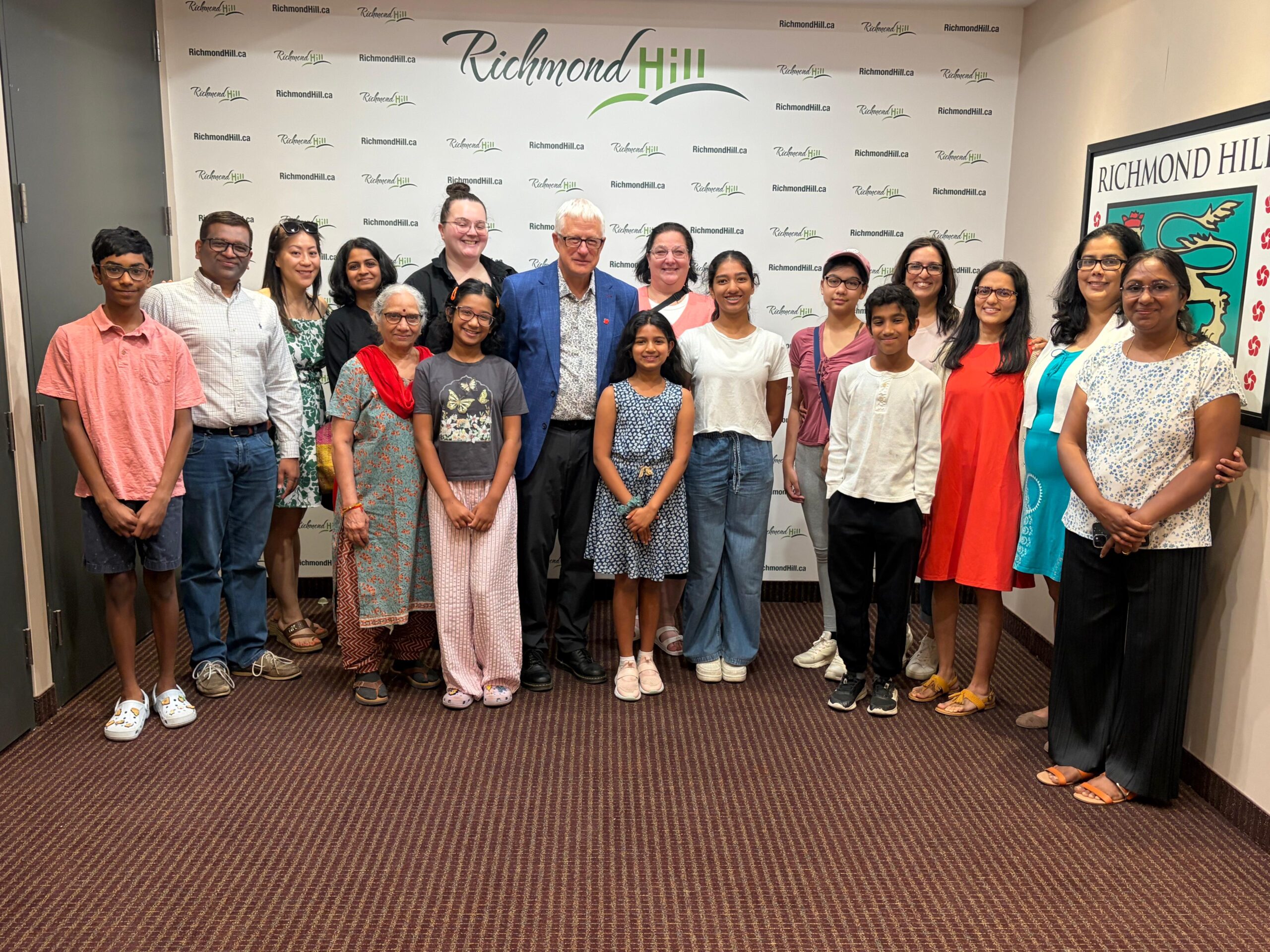 Group photo of Katya Gampa, her family, coaches and Richmond Hill Mayor David West standing together in front of a Richmond Hill step-and-repeat backdrop after a scroll presentation.